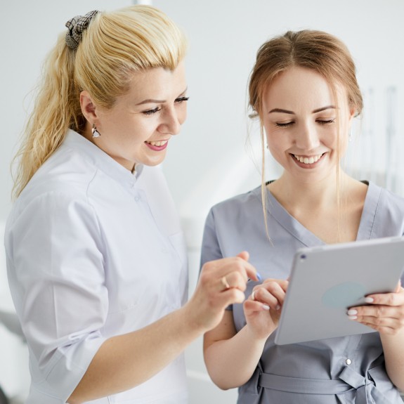 ZFA und Zahnärztin schauen gemeinsam in ein Tablet