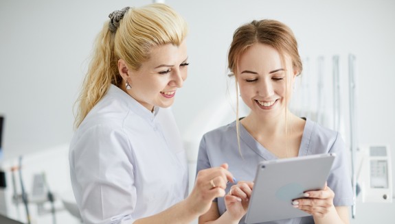 ZFA und Zahnärztin schauen gemeinsam in ein Tablet